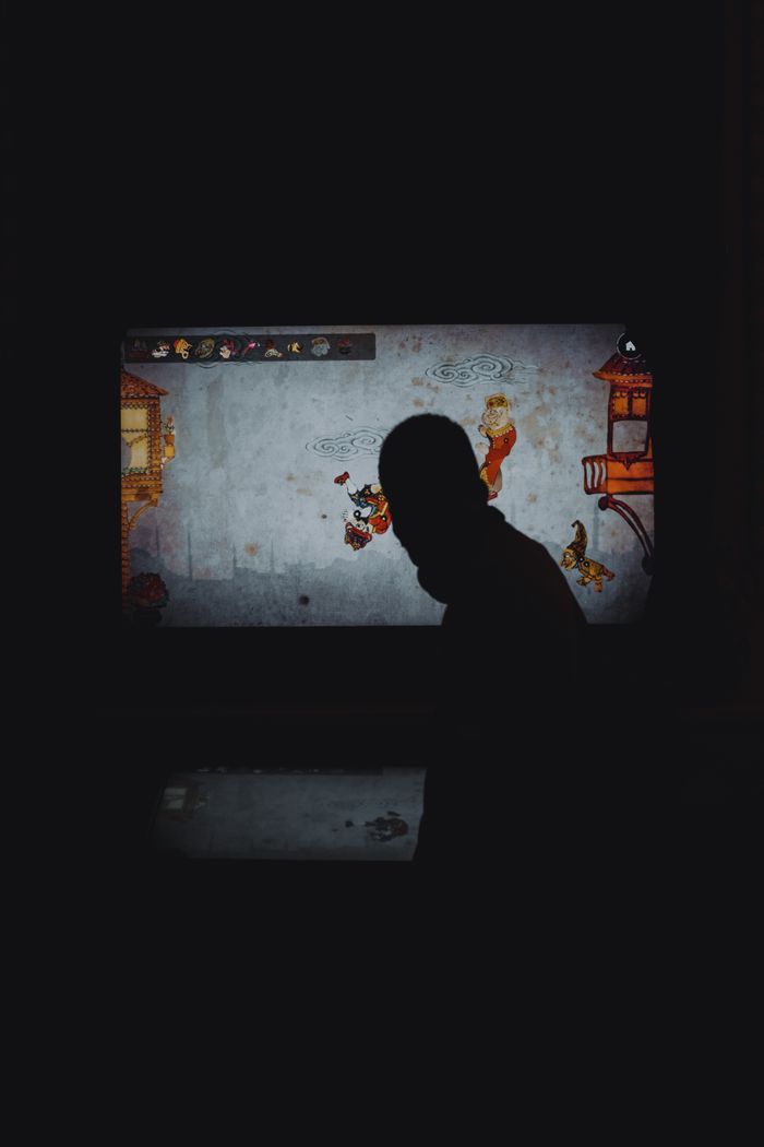 A persons silhouette in front of a colorful video game display in low light.